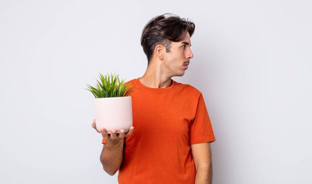 young hispanic man on profile view thinking, imagining or daydreaming. decorative plant concept - Zdjęcie, obraz