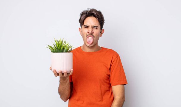 young hispanic man feeling disgusted and irritated and tongue out. decorative plant concept - Fotoğraf, Görsel
