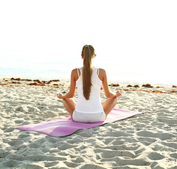 Woman doing yoga on the beach at sunrise - 写真・画像