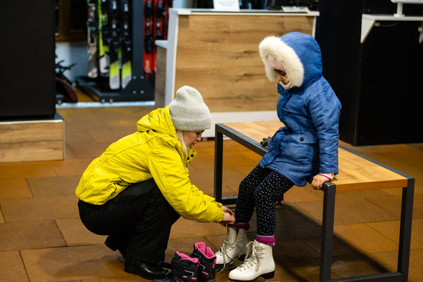 La mujer está ayudando a su hija a ponerse sus patines antes de llevarla a una clase de patinaje
. - Foto, Imagen