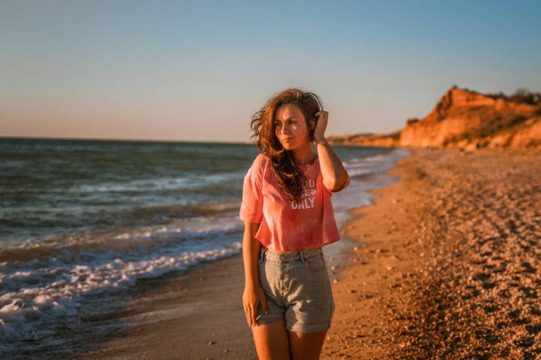 Молода красива жінка гуляє уздовж пляжу і захоплюється морем на заході сонця
 - Фото, зображення