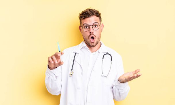 young handsome man feeling extremely shocked and surprised. physician syringe concept - Fotoğraf, Görsel