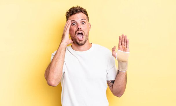 young handsome man screaming with hands up in the air. hand bandage concept - Foto, Bild