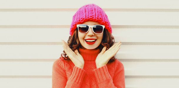 Winter portrait of happy smiling surprised young woman wearing a knitted sweater, pink hat having fun on white background - 写真・画像