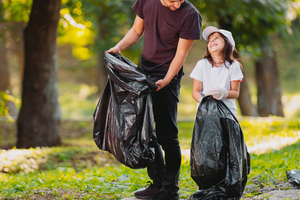 Smiling beautiful girl and adult man volunteer gathering rubbish together outdoors in gloves using garbage bags. - Valokuva, kuva