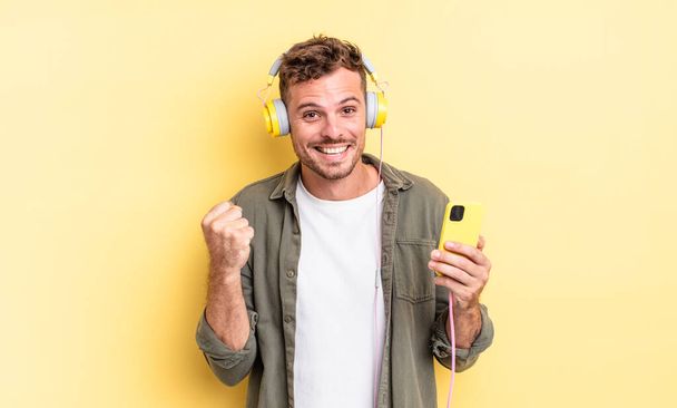 young handsome man feeling shocked,laughing and celebrating success headphones and smartphone concept - Foto, immagini