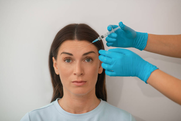 Une femme d'âge moyen aux cheveux bruns ayant une procédure d'injection battante - Photo, image