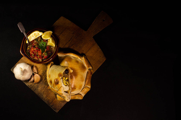 Зверху на стіл з емпанадами і чашею з пебром на чорному тлі, традиційною чилійською стравою. - Фото, зображення