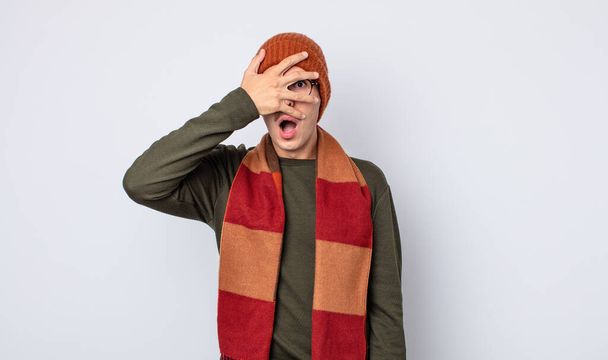 mladý pohledný muž, který vypadal šokovaně, vyděšeně nebo vyděšeně, zakryl tvář rukou. zimní oblečení koncept - Fotografie, Obrázek