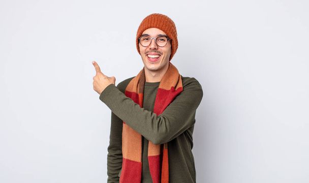 young handsome man looking excited and surprised pointing to the side. winter clothes concept - Foto, afbeelding
