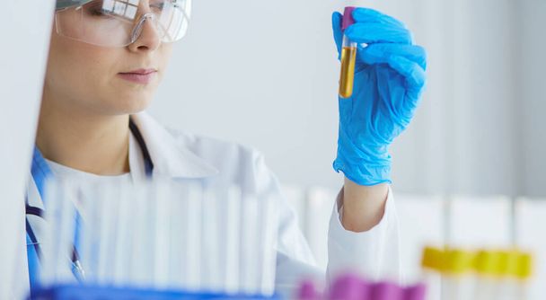 A female medical or scientific researcher or woman doctor looking at a test tube of clear solution in a laboratory - Foto, Bild