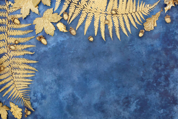 Borda de folha de ouro com samambaia, sicômoro, bolota e folhas de azevinho com nozes de bolota soltas no fundo azul manchado. Vista superior, flat lay, Outono, Samhain, Outono, Composição da natureza de Ação de Graças. - Foto, Imagem