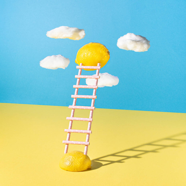 Floating lemons with ladders made of juice straw against yellow and blue background. Minimal summer natural concept. - Photo, Image