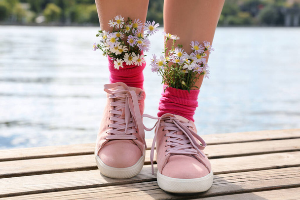 Woman with beautiful tender flowers in socks on wooden pier, closeup - Фото, зображення