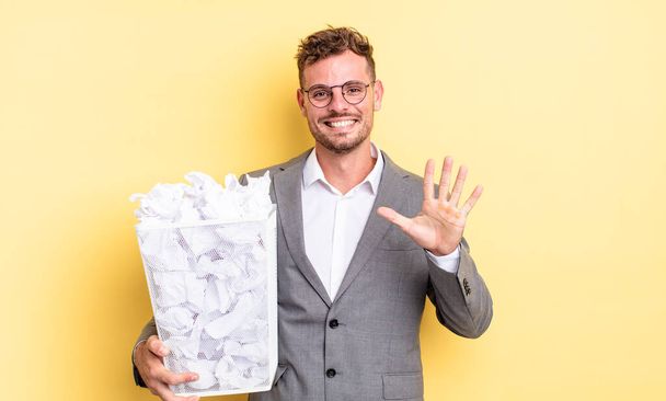 young handsome man smiling and looking friendly, showing number five paper balls trash concept - Фото, зображення