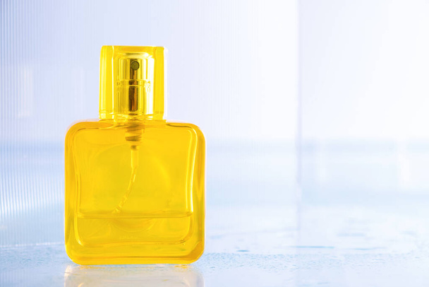 Lege gele fles parfum over blauwe keramische tegel achtergrond met druppels water - Foto, afbeelding