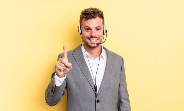young handsome man smiling and looking friendly, showing number one. telemarketer concetp - Fotografie, Obrázek