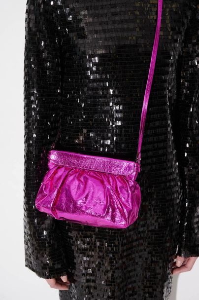 Κορίτσι με μαύρη πούλιες φόρεμα με γυαλιστερή φούξια ροζ δερμάτινη τσάντα. Βραδινό κόμμα εμφάνιση με κομψό συμπλέκτη. Τσάντα με λεπτομέρειες. Κοντινό πλάνο. Κάθετη φωτογραφία. - Φωτογραφία, εικόνα