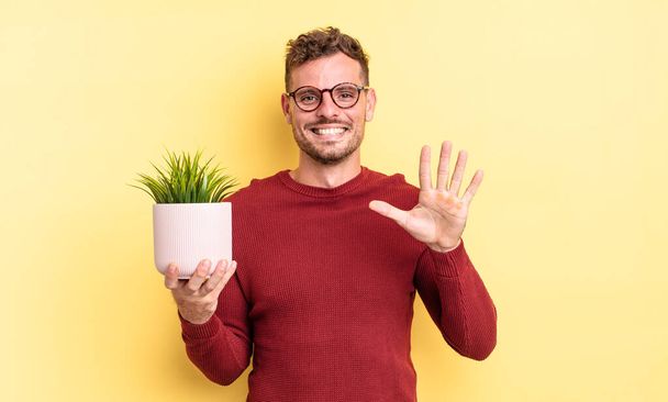 young handsome man smiling and looking friendly, showing number five. decorative plant concept - Фото, зображення