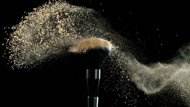 Soft cosmetics brush releasing a cloud of beige face powder over a black background with copy space. Beauty and makeup concept - Photo, image