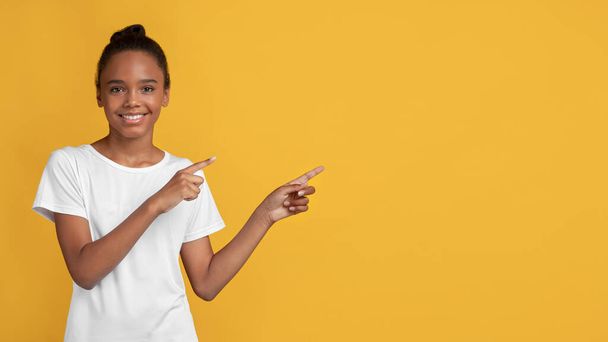 Boldog mosolygós tini fekete lány fehér pólóban ujjal mutogatva a szabad térbe - Fotó, kép