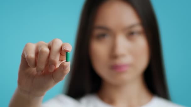 Čínská dáma ukazuje medicína pilulku na kameru na modrém pozadí - Záběry, video