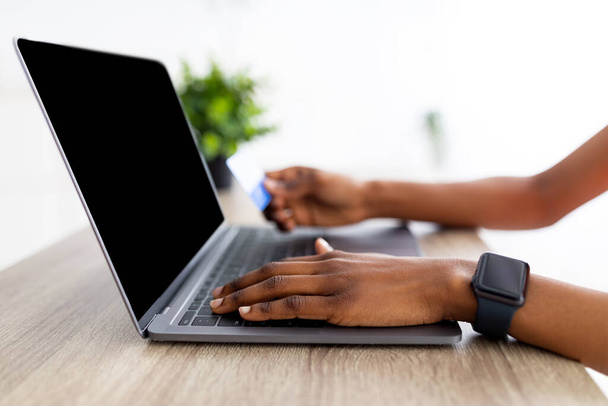 Gros plan de dame noire à l'aide d'un ordinateur portable et carte de crédit pour faire des achats en ligne à partir de la maison, maquette pour le site de shopping à l'écran - Photo, image