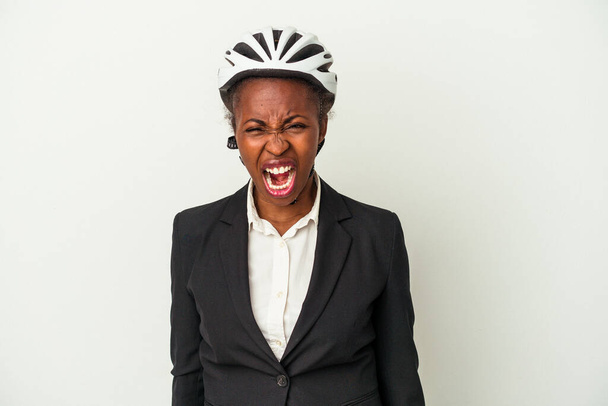Mujer afroamericana de negocios joven con un casco de bicicleta aislado sobre fondo blanco gritando muy enojado y agresivo. - Foto, Imagen