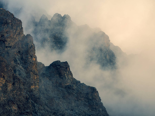 М'який фокус. Небезпечна ущелина. Драматичний туман серед гігантських скелястих гір. Примарний атмосферний вид на велику скелю в хмарному небі. Низькі хмари і красиві хмари. Мінімалістичні пейзажі загадкове місце
. - Фото, зображення