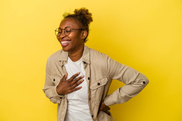 Молодая африканская американка изолирована на желтом фоне смеясь держа руки на сердце, концепция счастья. - Фото, изображение
