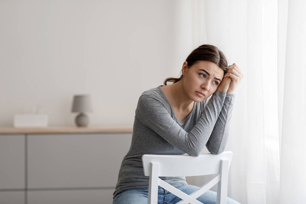 Θλιβερό άγχος απογοητευμένη γυναίκα χιλιετή έχει ψυχική διαταραχή, προβλήματα και κακό συναίσθημα, κάθεται στην καρέκλα μόνη της - Φωτογραφία, εικόνα
