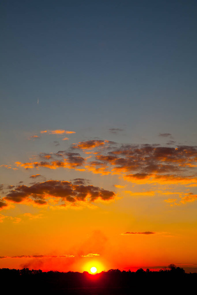 Zachodzące słońce podświetla małe chmury pomarańczowo-białymi - Zdjęcie, obraz