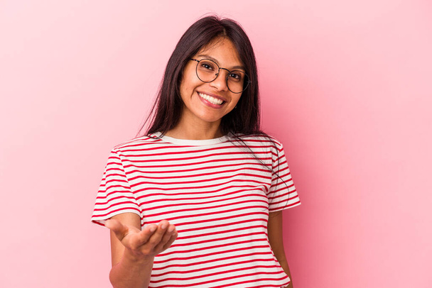 Молодая латинская женщина на розовом фоне протягивает руку к камере в приветственном жесте. - Фото, изображение