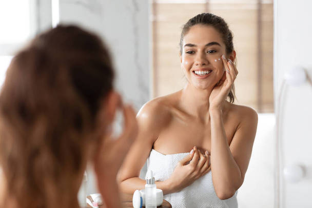 Weibliche Pflege für die Haut feuchtigkeitsspendende Gesicht mit Creme im Badezimmer - Foto, Bild