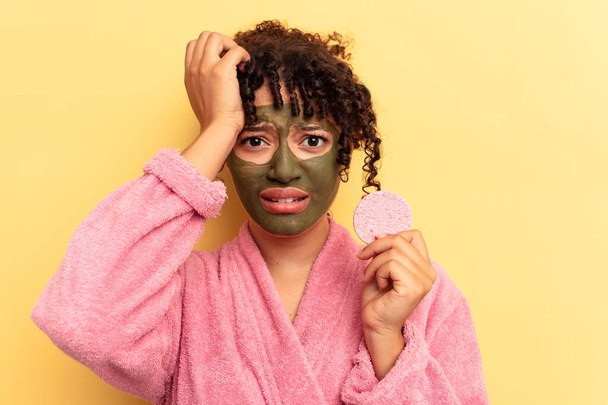 Young mixed race woman wearing a bathrobe holding a make-up remover sponge isolated on yellow background being shocked, she has remembered important meeting. - Foto, immagini