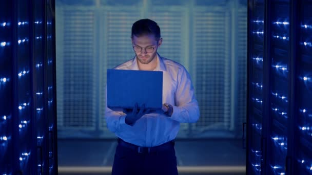 A férfi hálózati mérnök rendszerellenőrzést végez a szerverszobában a laptopjával. Az adatközpontban férfiak szerver szakemberek ellenőrzése munkarendszer és hardver rack szerver számítógép szekrények - Felvétel, videó