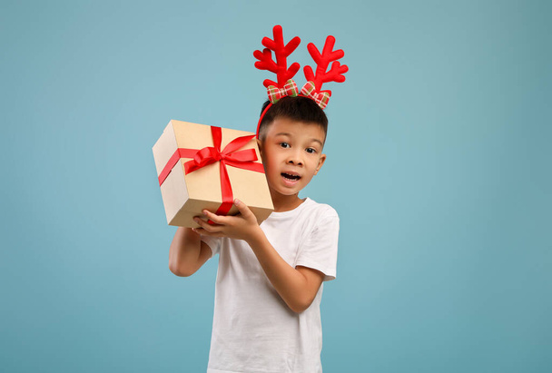 Возбужденный маленький азиатский мальчик носит рождественские оленьи рога холдинг настоящее Box - Фото, изображение