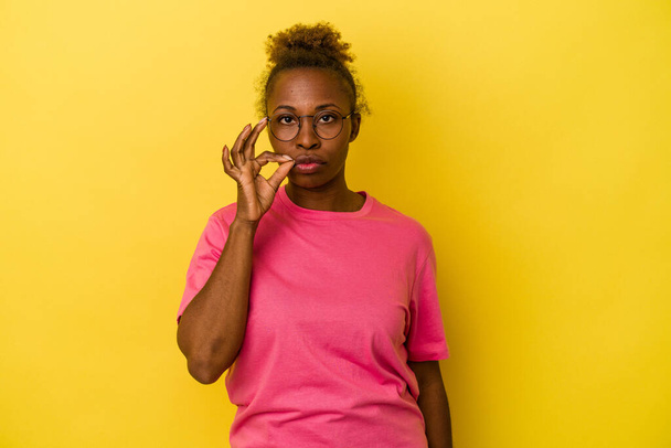 Young african american woman isolated on yellow background with fingers on lips keeping a secret. - Фото, зображення