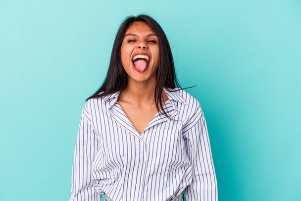 Young latin woman isolated on blue background funny and friendly sticking out tongue. - Photo, Image