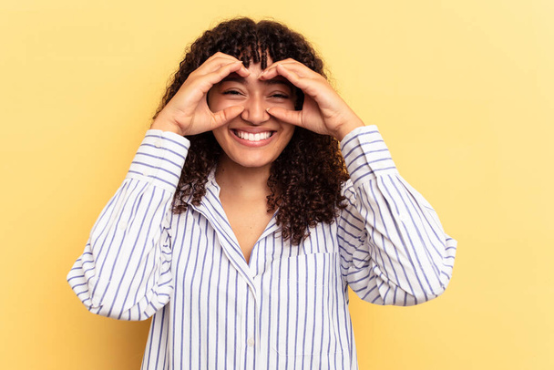 Young mixed race woman isolated on yellow background showing okay sign over eyes - Foto, Bild
