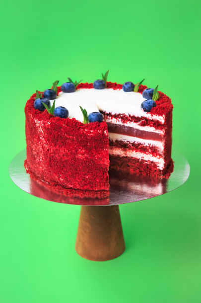 Κομμένη τούρτα γενεθλίων στο ξύλινο περίπτερο κέικ. Κόκκινο βελούδινο κέικ διακοσμημένο με φύλλα μέντας και βατόμουρα. Πράσινο φόντο. Αντιγραφή χώρου. Φωτογραφία τροφίμων για συνταγή. - Φωτογραφία, εικόνα