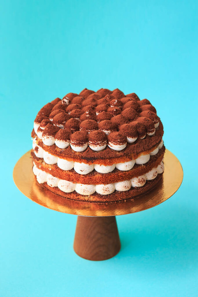 Tort urodzinowy na drewnianym stoisku z tortem. Piękne ciasto czekoladowe z bitą śmietaną ozdobione posypką kakao. Niebieskie tło. Odbiór. Fotografia żywności dla przepisu. - Zdjęcie, obraz