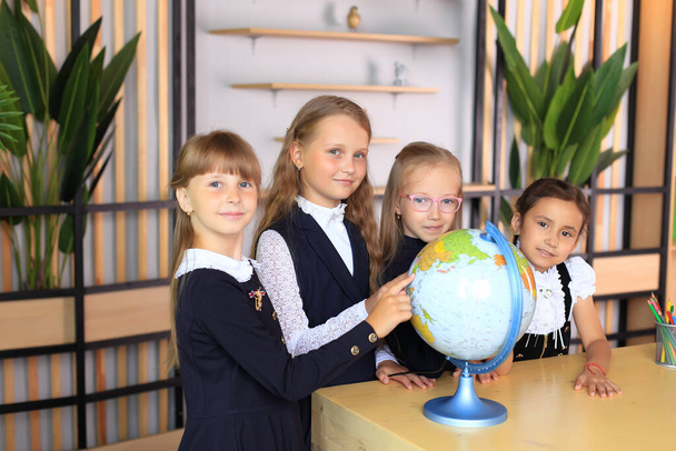 Des enfants en uniforme scolaire avec un globe dans le bureau. - Photo, image