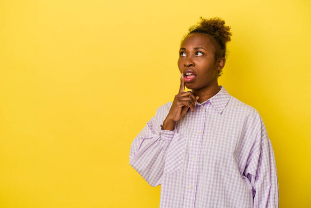 Giovane donna afroamericana isolata su sfondo giallo guardando lateralmente con espressione dubbia e scettica. - Foto, immagini