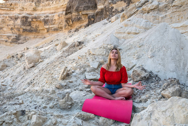 jolie jeune femme faire des exercices de yoga relax avec tapis sur sable sec parmi les carrières vides - Photo, image