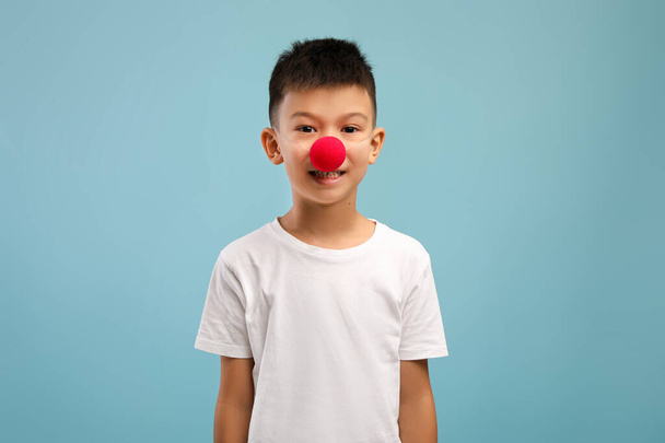 Zabawny mały azjatycki chłopiec w czerwonych klaunów nos i patrząc w aparat - Zdjęcie, obraz