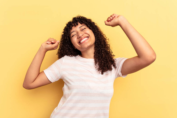 Mujer joven de raza mixta aislada sobre fondo amarillo celebrando un día especial, salta y levanta los brazos con energía. - Foto, imagen