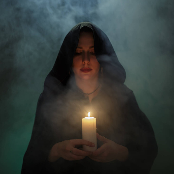 woman witch is holding a burning candle. Mysterious smoke - Photo, Image