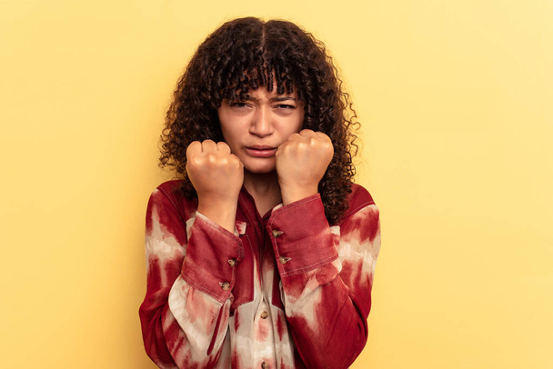 Young mixed race woman isolated on yellow background showing fist to camera, aggressive facial expression. - Photo, Image