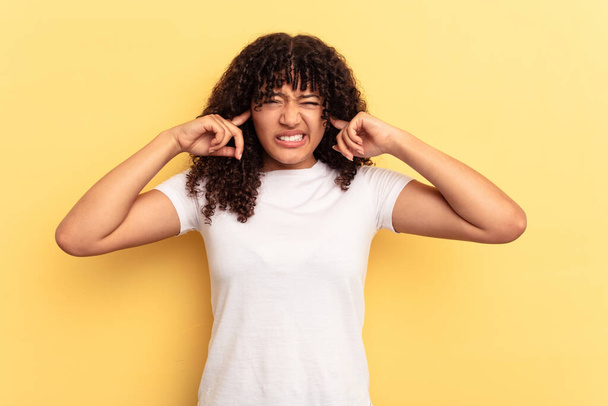 Junge Frau mit gemischter Rasse isoliert auf gelbem Hintergrund, die Ohren mit Fingern bedeckt, gestresst und verzweifelt durch ein lautes Ambiente. - Foto, Bild